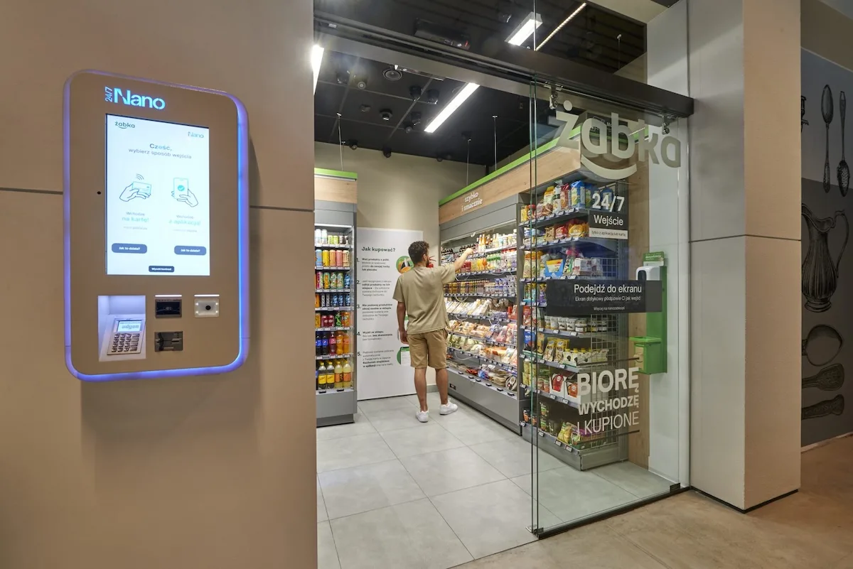 Sklep autonomiczny Żabka Nano z klientem wybierającym produkty z półki – nowoczesna przestrzeń sprzedaży bezobsługowej. Zdjęcie ilustruje temat postępowania prowadzonego przez Urząd Ochrony Konkurencji i Konsumentów, które dotyczy m.in. sposobu komunikowania promocji i informowania o cenach.