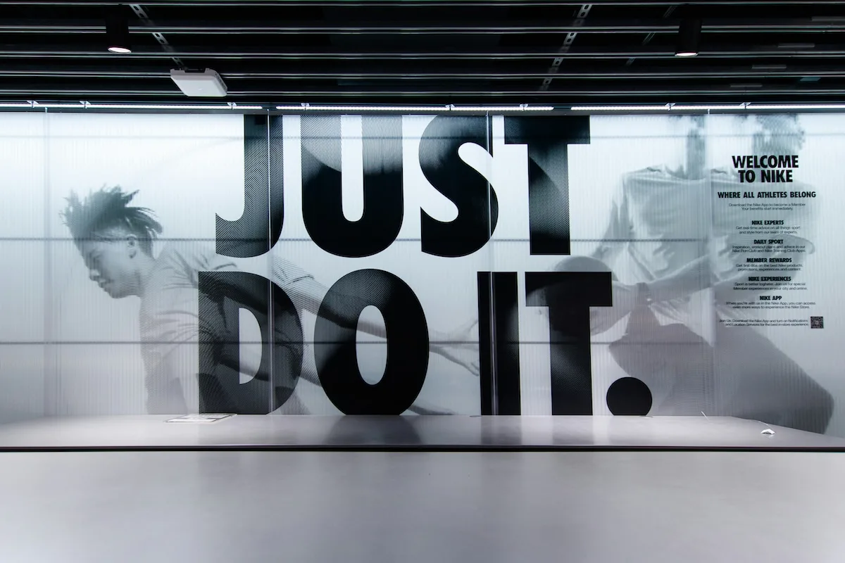 Witryna sklepu Nike z dużym napisem „Just Do It” oraz grafiką przedstawiającą sportowców. Nowoczesna ekspozycja promuje sportowy styl życia i produkty marki.