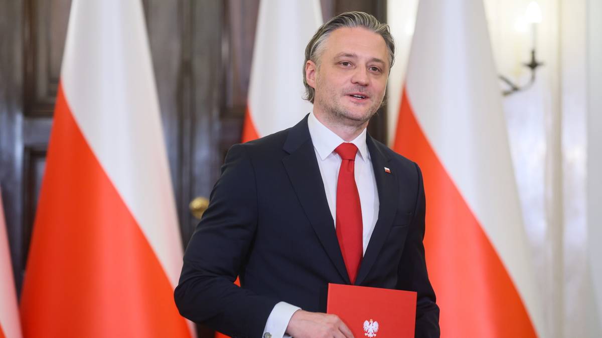 Mężczyzna w garniturze i krawacie trzyma czerwony folder.