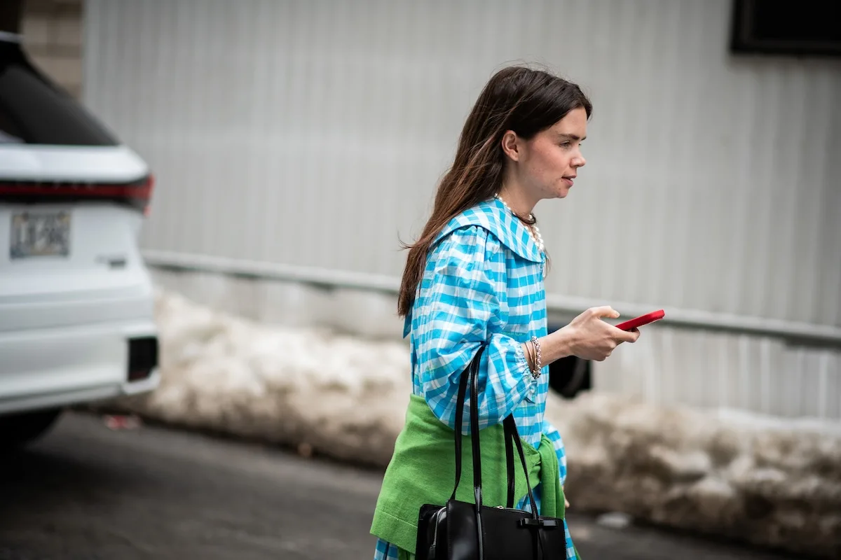 Kobieta w barwnym stroju korzystająca ze smartfona podczas spaceru po mieście – symbol powiększającej się roli social commerce w fast fashion. Zakupy modowe coraz częściej mają miejsce online i są inspirowane mediami społecznościowymi. Obraz pokazuje, jak technologia i trendy wpływają na postęp rynku fast fashion.