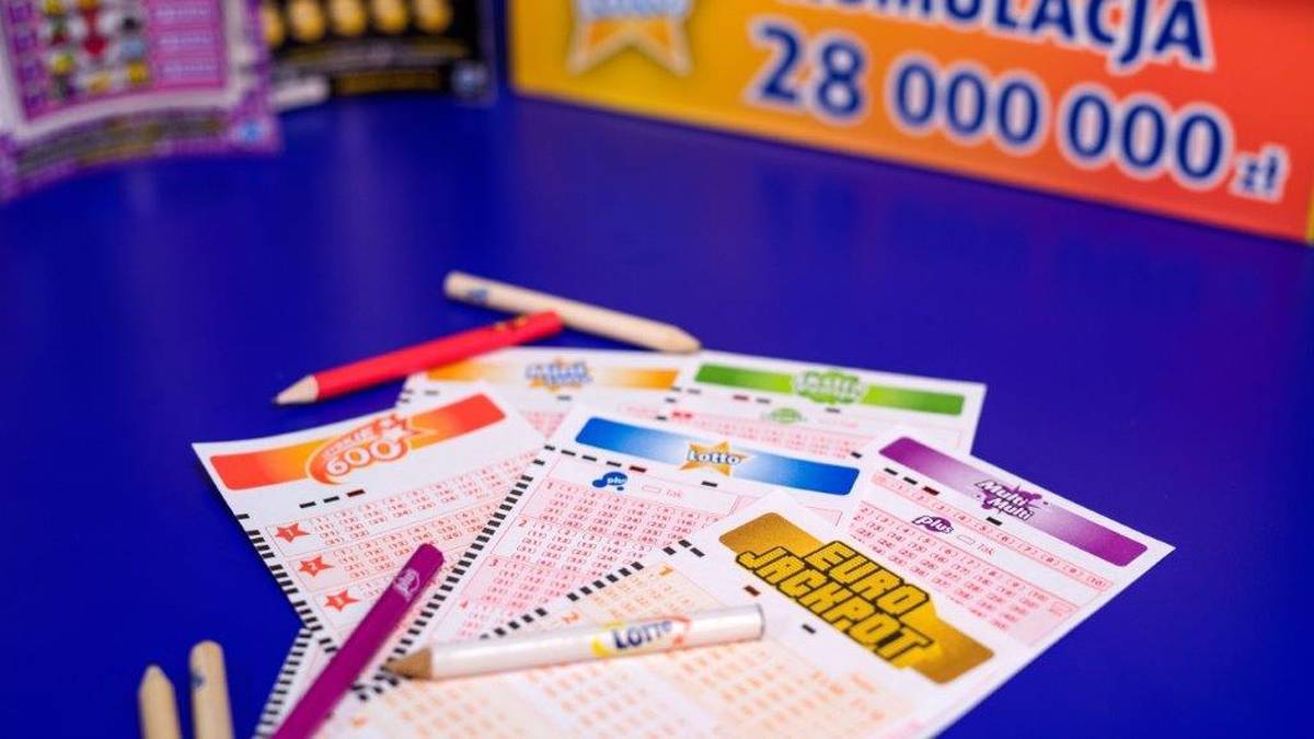 Kupony gier liczbowych Lotto i Eurojackpot na niebieskim tle, obok kredki, w tle baner z informacją o kumulacji