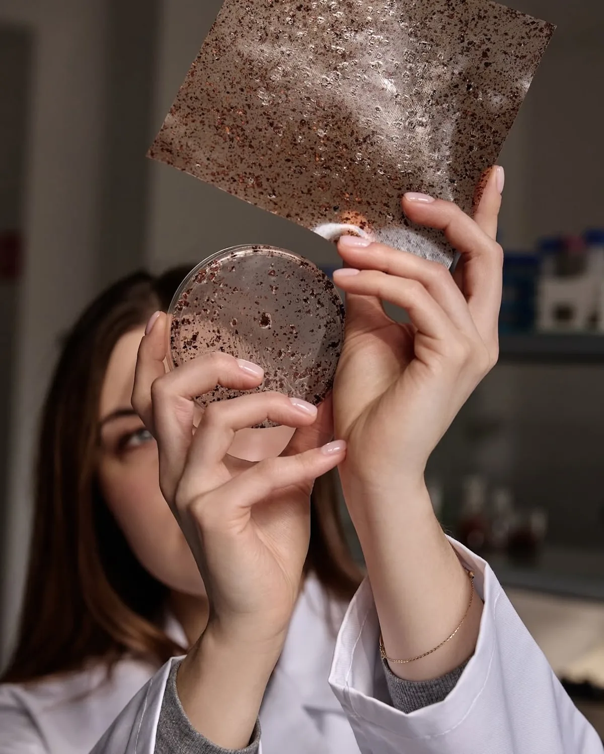 Osoba w laboratorium prezentuje próbki innowacyjnego materiału NUTICO® na bazie łusek kakaowca i łupin orzechów. Zdjęcie pokazuje etap prac nad polską „czekoladową skórą”, nagrodzoną PETA Vegan Fashion Award 2026.