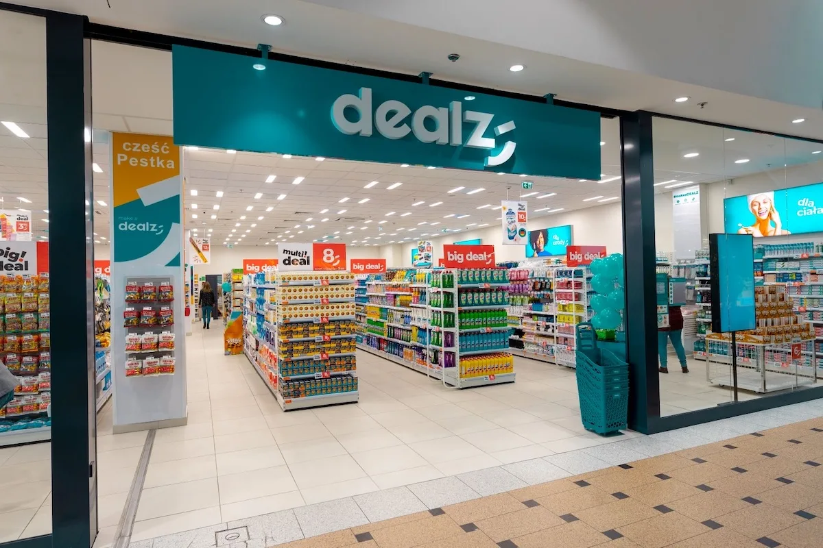 Wejście do sklepu Dealz w centrum handlowym, z widocznym szyldem marki i alejkami pełnymi produktów. Sieć Dealz Poland ma zmienić właściciela w ramach transakcji z Pepco Group i brytyjskim funduszem Modella Capital.