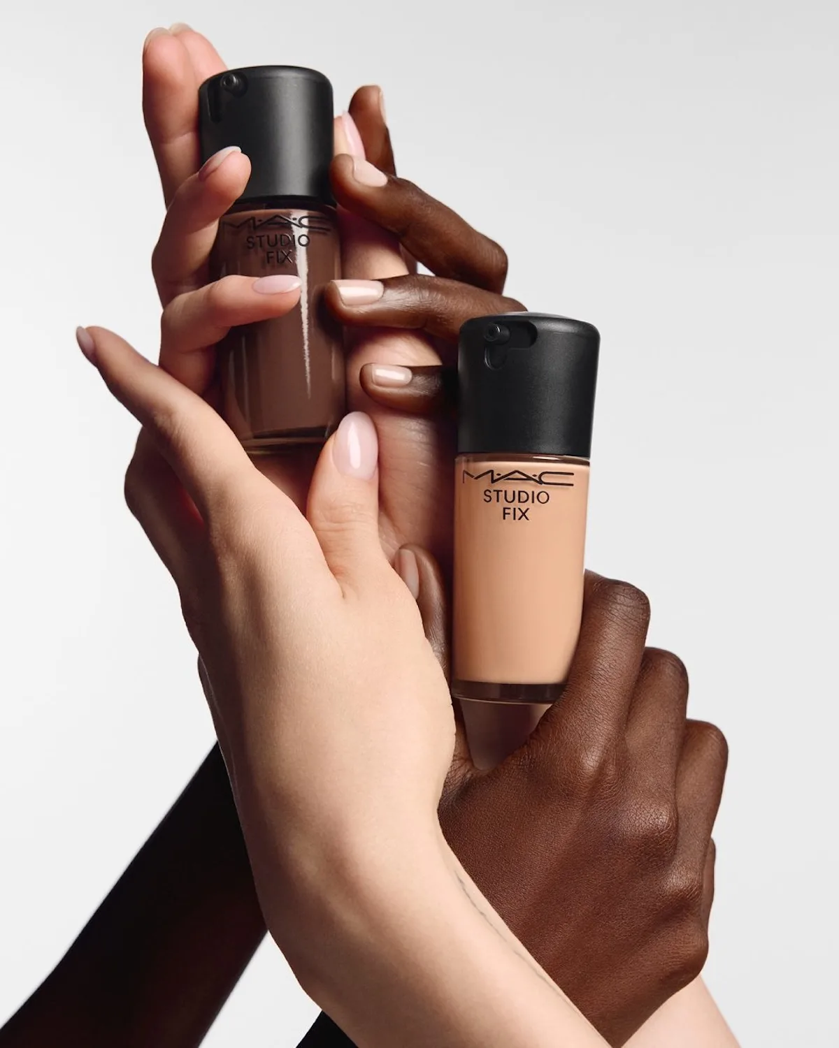 Na zdjęciu widać dwa podkłady MAC Studio Fix trzymane w dłoniach osób o różnych odcieniach skóry. Fotografia nawiązuje do artykułu o pozwie przeciwko MAC Cosmetics, technologii virtual try-on i zarzutach dotyczących prywatności użytkowników.
