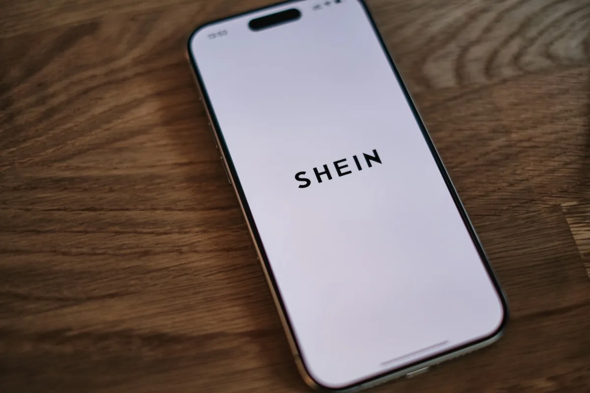 Logo Shein wyświetlane na ekranie smartfona. Chiński gigant ultra fast fashion ponownie znalazł się pod presją europejskich regulatorów po tym, jak Francja nałożyła na platformę ponad 22 mln euro kary za naruszenia praw konsumentów i brak transparentności.