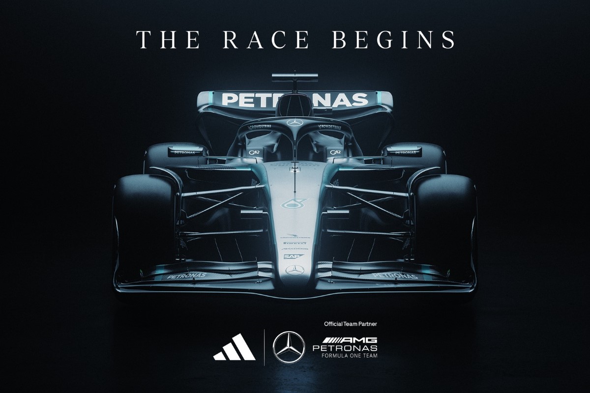 Na zdjęciu widzimy futurystyczny bolid Mercedesa F1 na ciemnym tle z napisem "The Race Begins" u góry. W dolnej części znajdują się logotypy Adidasa, Mercedesa i AMG Petronas Formula One Team, symbolizujące nowe partnerstwo. Obraz podkreśla wejście marki Adidas w F1, łącząc technologię, styl i innowacje w świecie motorsportu.