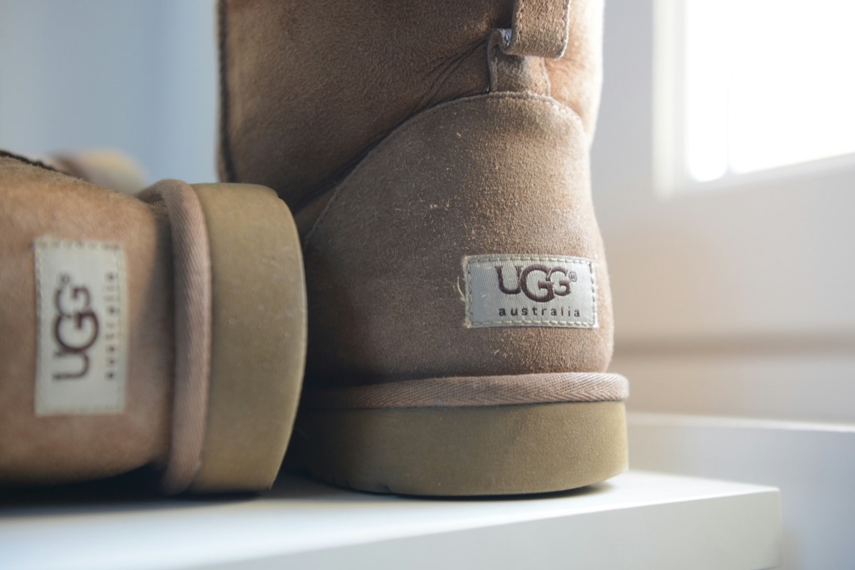 Na zdjęciu widać parę butów marki UGG, popularnych na całym świecie, z charakterystycznym logiem „UGG australia” na boku. Buty w odcieniach beżu wykonane z miękkiego zamszu są symbolem komfortu i ciepła, które zyskały ogromną popularność wśród miłośników mody. UGG stało się marką rozpoznawalną globalnie, oferującą produkty łączące funkcjonalność z modnym designem.