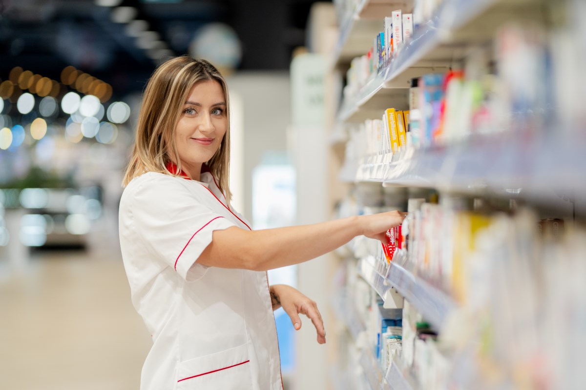 Zdjęcie przedstawia uśmiechniętą pracownicę drogerii Rossmann, która porządkuje produkty na półce sklepowej. Profesjonalizm i zaangażowanie pracowników to jeden z kluczowych czynników wpływających na rekordowe wyniki sieci Rossmann, które w 2024 roku osiągnęły najwyższe obroty w historii firmy.